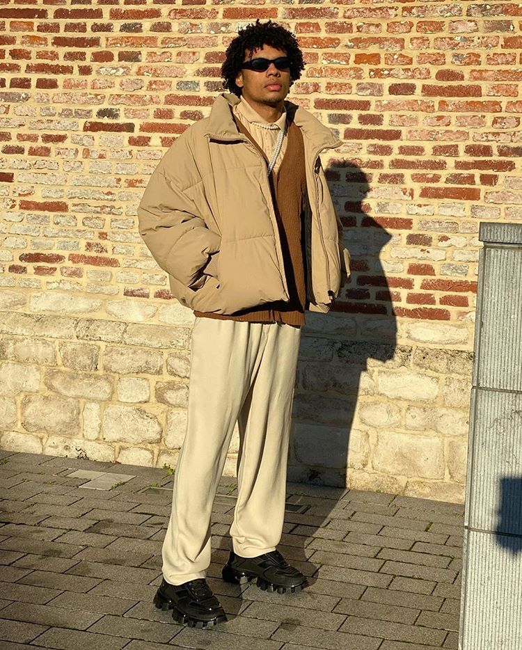 Style reference: a tan puffer jacket and cream trousers against a brick wall